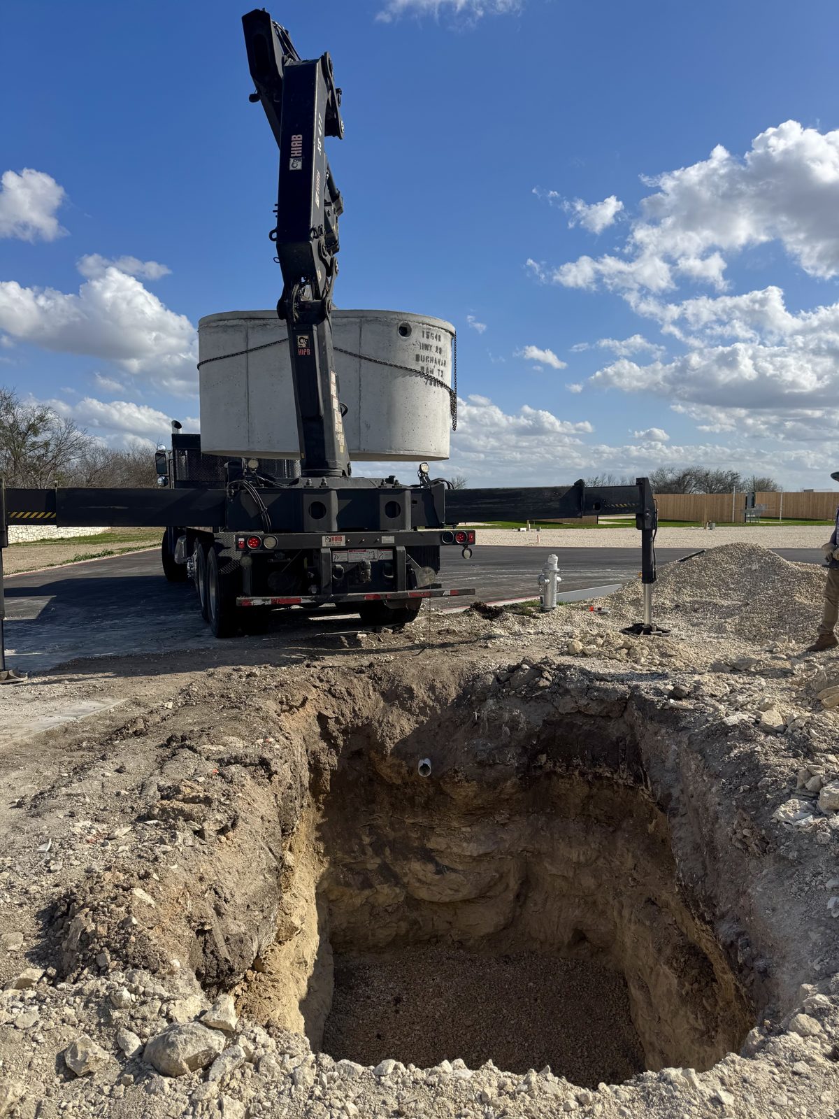 Crane truck lowering a concrete septic tank into a freshly dug hole